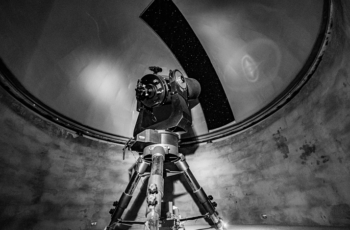 Telescope pointing at the sky in an observatory with the dome open and stars visible