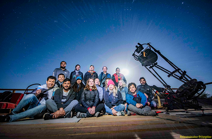 Group sitting under a starry sky next to a telescope during astrophotography activity