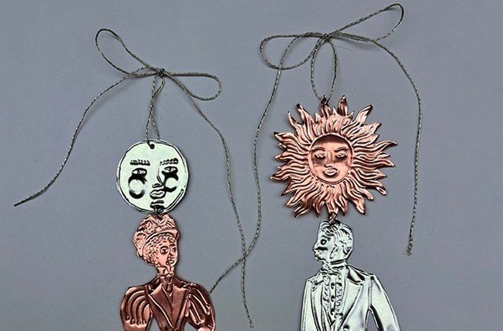 Pair of handcrafted embossed decorations in silver and copper tones, showing a moon face and sun face above elegantly dressed figurines. 