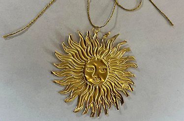 Gold embossed aluminium sun pendant with a human face at its centre, suspended on a twisted gold cord.