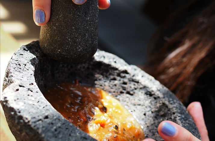 Close-up of hands grinding salsa in a stone molcajete during an immersive mezcal and Mexican culture experience.