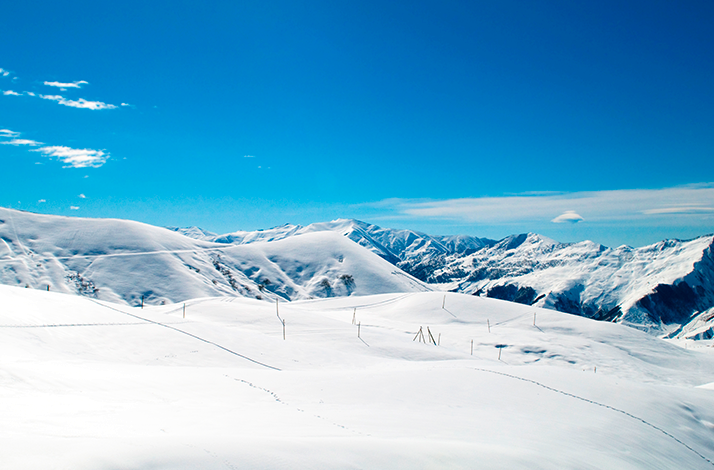 Pristine white slopes and alpine peaks in the Andes under a bright blue sky.