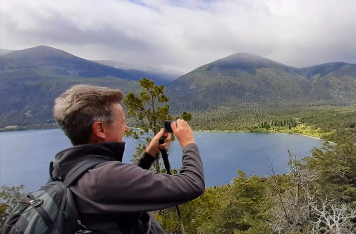 Hiker photographing a panoramic lake and forest view