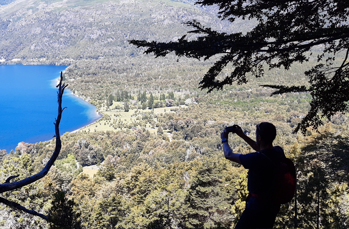 Hiker capturing a scenic lake and forest from a high viewpoint