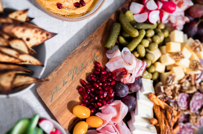 Charcuterie board with meats, cheeses, olives, pickles, and pomegranate.