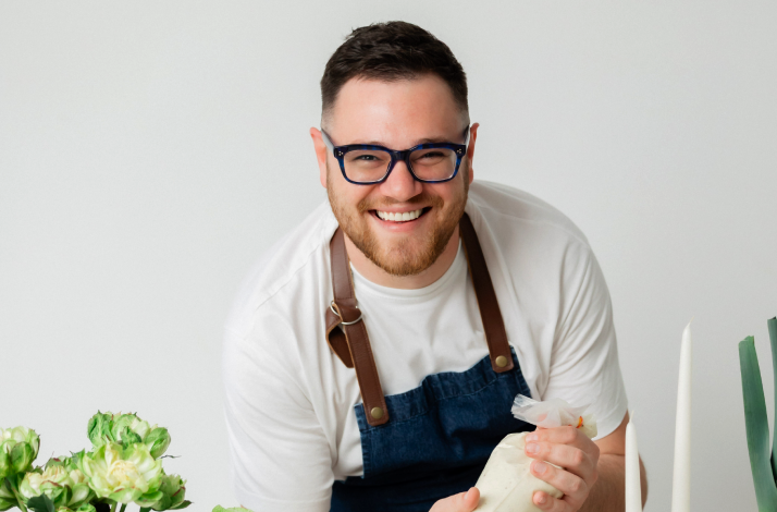Chef Mile in a white shirt and apron piping cream, surrounded by fresh greens.
