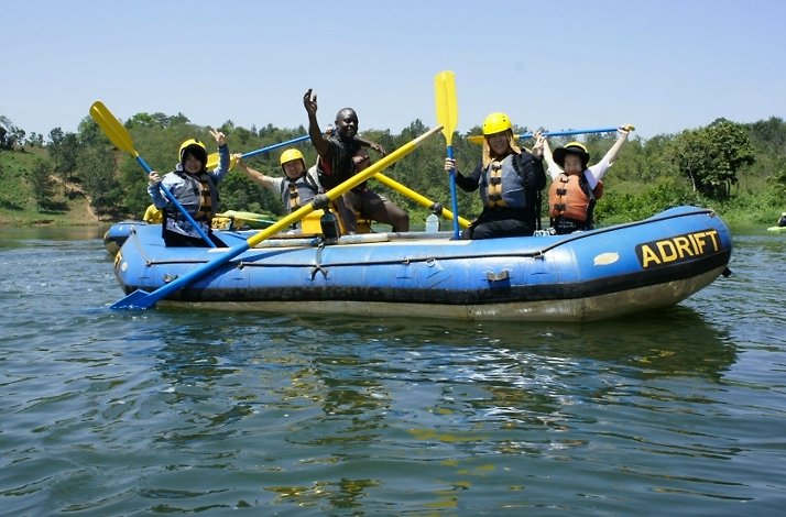Group of rafters celebrating on calm waters during their Nile River experience, holding paddles aloft.