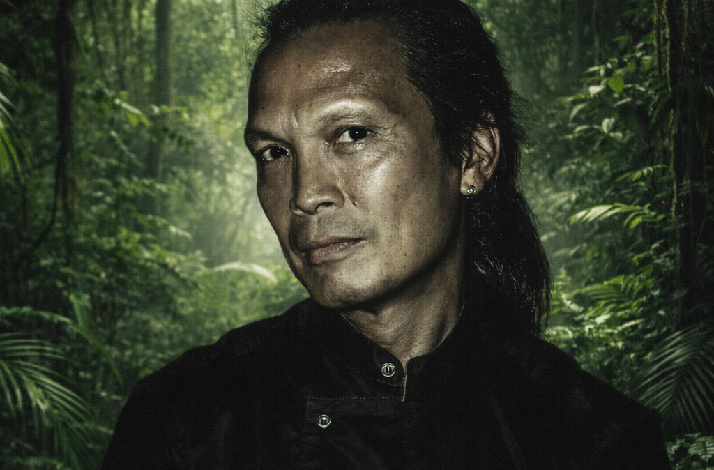 Celebrity chef Susur Lee posing in a dark high-collared shirt against a lush jungle backdrop.