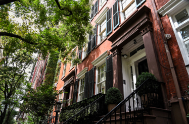 Tree-lined street in Greenwich Village, New York City, featuring classic red-brick rowhouses known as brownstones. 
