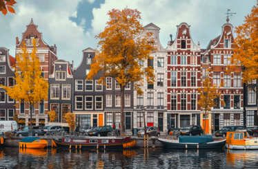 Canal houses and boats in Amsterdam with autumn trees.