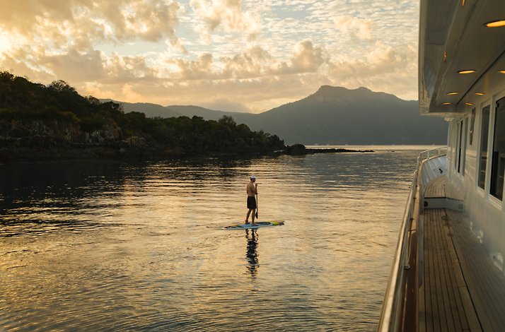 Stand‑up paddleboarding beside the yacht at sunset.