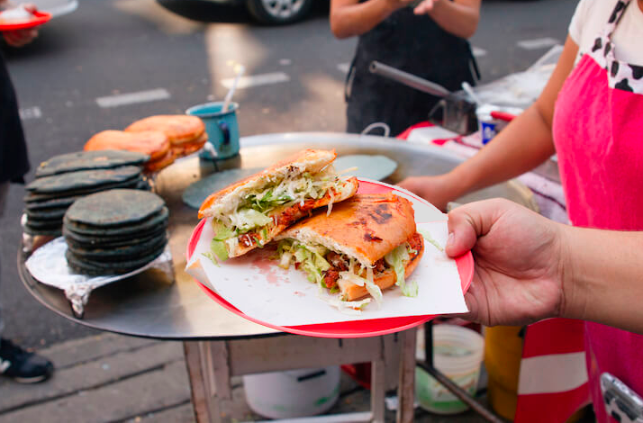 Freshly prepared Mexico City street food served at a sidewalk stand, featuring a filled tortilla and traditional accompaniments.