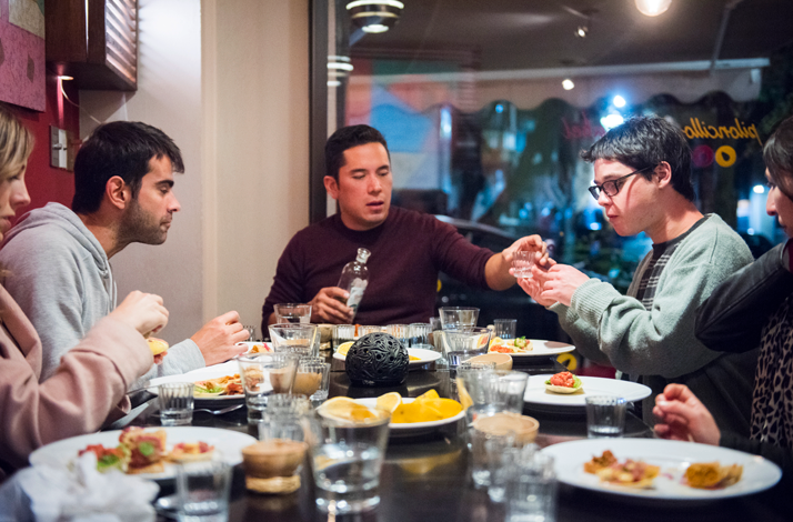 Small group sharing tacos and mezcal around a table indoors.