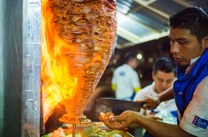Spit-roasted al pastor meat being sliced directly into a tortilla.