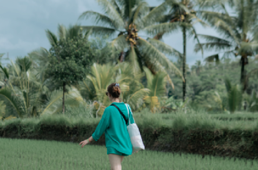 A woman in a bright green oversized top walks through a Jatiluwih Rice Terraces in Bali, Indonesia.