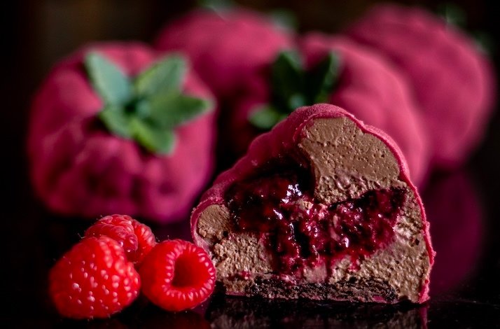 Cross-section of a raspberry-shaped mousse dessert with chocolate and raspberry filling.