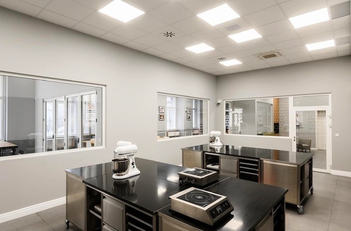 Modern pastry kitchen with stainless steel workstations and mixers.