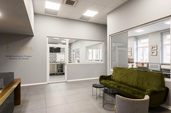 Reception area with a green sofa, tables, and a view into the pastry kitchen.