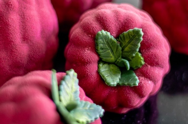 Close-up of raspberry-shaped mousse desserts with detailed green leaves.