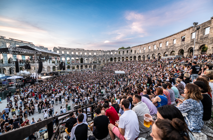 Packed concert crowd seated in the ancient stone tiers and standing on the floor of the Pula Arena in Pula, Croatia.