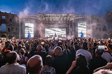 A large crowd watches a live concert at night inside the ancient Roman Pula Arena in Pula, Croatia.