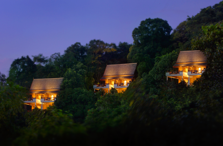 Hilltop villas glowing warmly at dusk, nestled among dense tropical trees at Pangkor Laut Resort.
