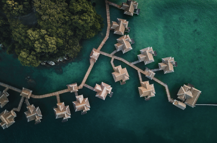 Overwater villas connected by wooden walkways, surrounded by lush forest and clear sea at Pangkor Laut Resort.
