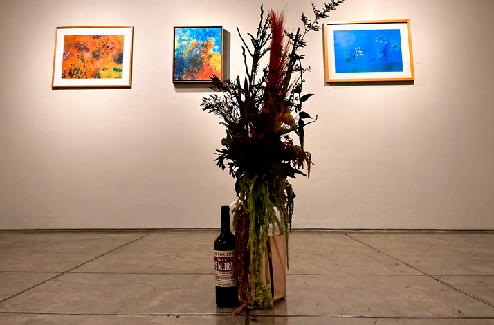 Bottles on the floor with flower arrangements at Galería Oscar Román.