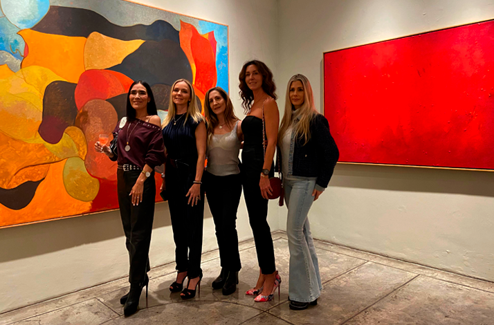 Group of women posing and sipping wine in front of large paintings at Galería Oscar Román.