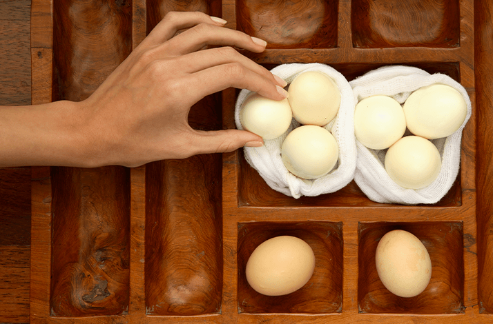 Person's hand reaching for eggs placed in a wooden egg tray at the Majestic Malacca Hotel in Malacca, Malaysia.