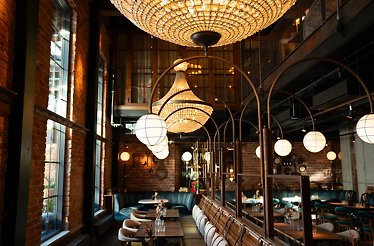 You step into a warm, softly lit restaurant where crystal chandeliers shimmer overhead, casting a gentle glow across wooden tables and velvet-covered sofas.