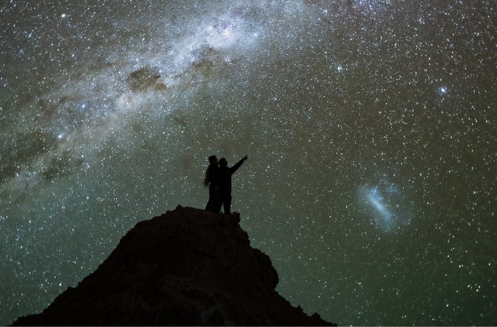 Two people pointing at the stars at Atacama Desert.