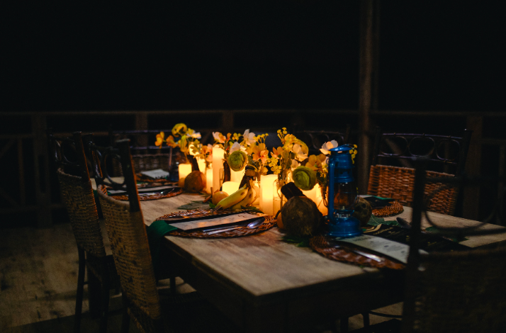 Elegantly set dining table at Tree House B&B, illuminated by candlelight with floral centerpieces and wicker chairs.