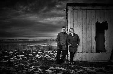 A black-and-white portrait of the owners behind RE-NAA, standing together by a weathered seaside cabin.
