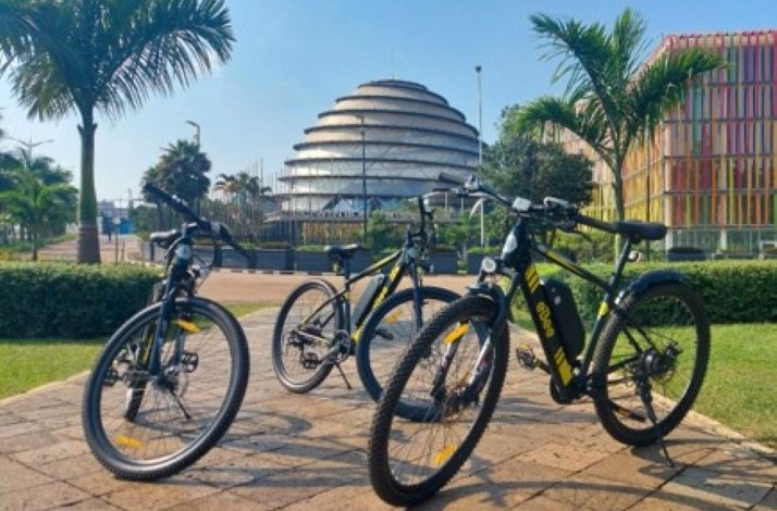 Three e-bikes parked in front of Kigali Convention Centre and palm trees.