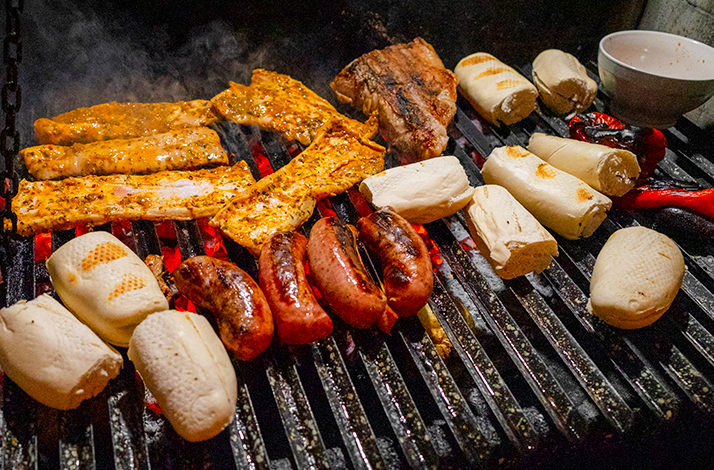 An Argentine grill loaded with sizzling meats, sausages, and bread over glowing hot coals.