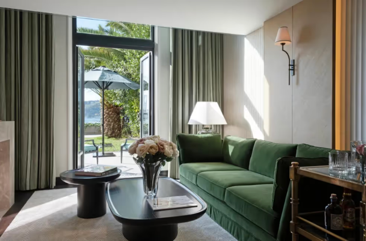 A serene living area featuring a green velvet sofa, stylish coffee tables, and large doors opening to a garden with a Bosphorus view and palm trees.