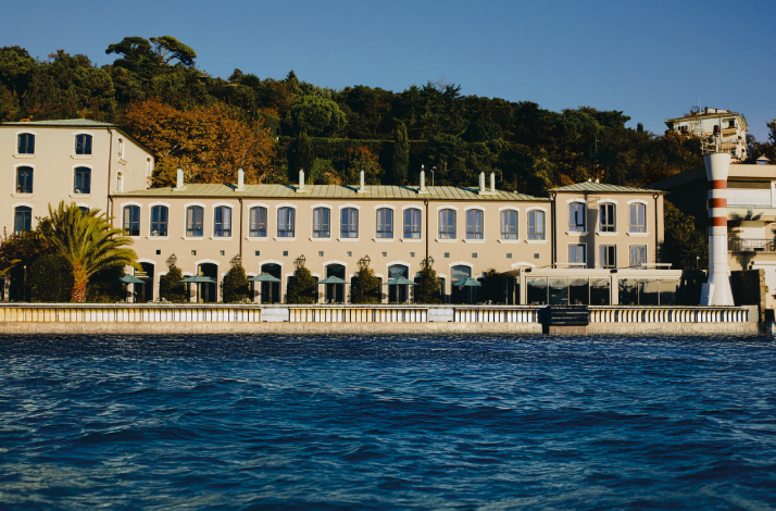 A panoramic waterfront view of a historic yellow building with classical architecture and a lighthouse, situated along the Bosphorus coast.