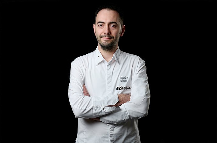 Chef Alessandro Bellingeri in a white coat with the Osteria Acquarol logo against a black background.