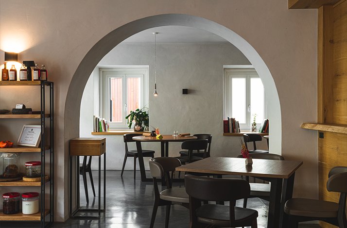 The minimalist interior of Osteria Acquarol restaurant featuring wooden tables and a large prominent arch.