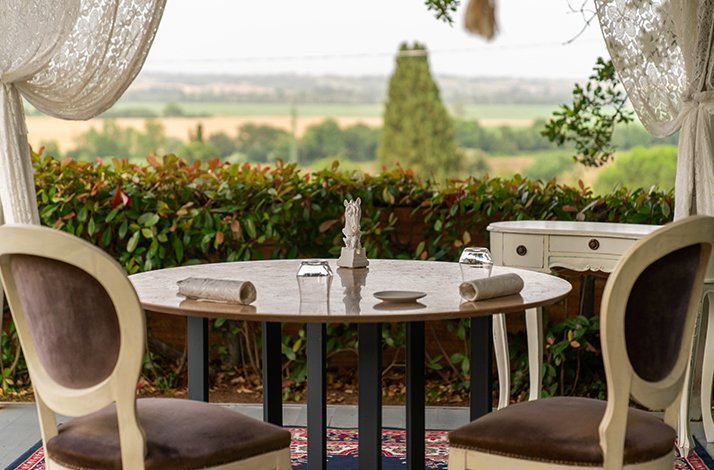 An elegant outdoor dining table framed by lace curtains, offering a scenic countryside view at La Sosta del Cavaliere.