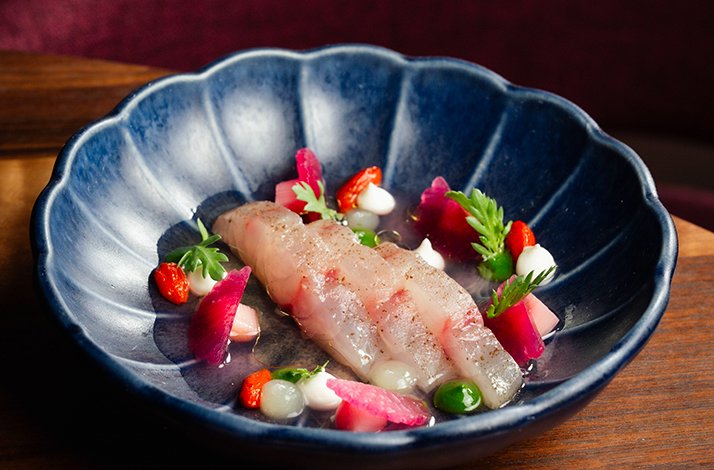 Raw fish course garnished with pickled vegetables, micro herbs, and dotted cream in a fluted blue bowl at Alo Restaurant.