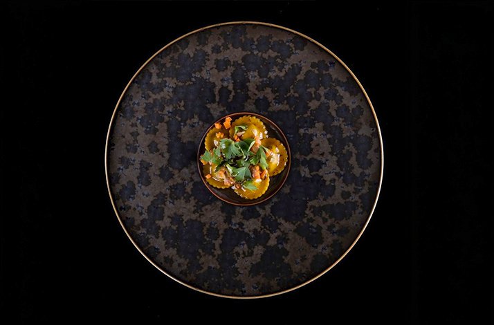 Artistic plating of ravioli pasta garnished with herbs and vegetables.