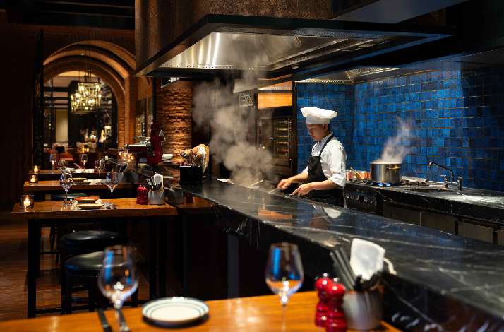 The chef is cooking, preparing food in an open kitchen concept at The Cellar at Grand Hyatt Manila.