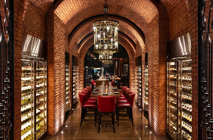 Grand Hyatt Manila wine cellar featuring red leather chairs, long wooden table, brick arches, and lit wine refrigerators.
