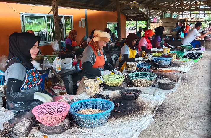 Row of women in headscarves and aprons working at a cashew nut processing station, sorting and preparing nuts in baskets.