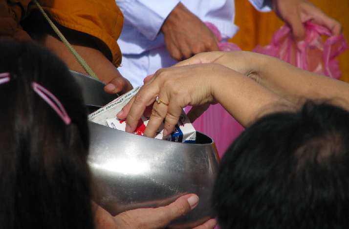 Hands offering items into a monk’s alms bowl during a Buddhist ritual.