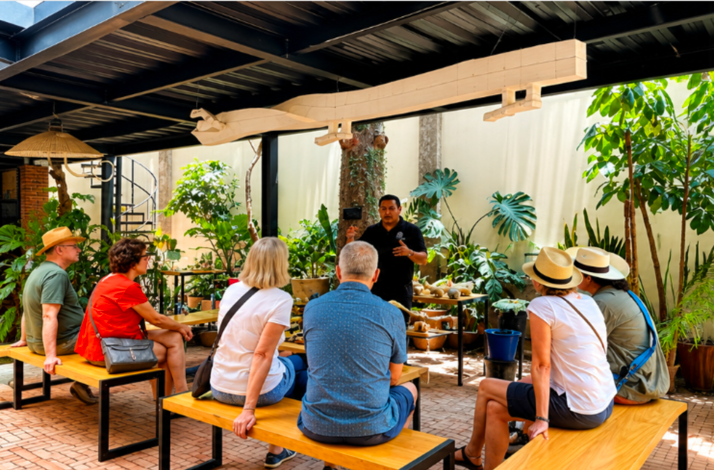 Guests listening to a guided introduction about Zapotec art in a lush open-air San Martín Tilcajete workshop.