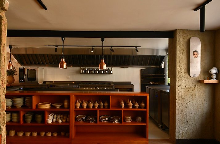 Open kitchen and dining area at Afluente in Bogota, Colombia, with copper pendant lights and wooden shelving displaying stacks of handmade ceramic bowls and plates
