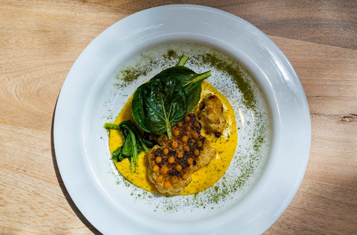 Plated dish at Carmen, Medellin: golden cauliflower and crispy lentils in a saffron-hued sauce with fresh greens on a white plate